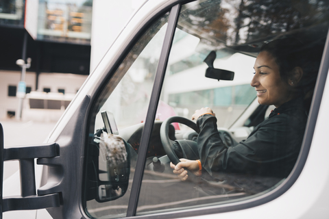 Lächelnde Frau fährt Lieferwagen in der Stadt, lizenzfreies Stockfoto