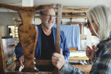 Älterer Eigentümer zeigt einem männlichen Kunden in der Werkstatt einen Holzstuhl - MASF00289