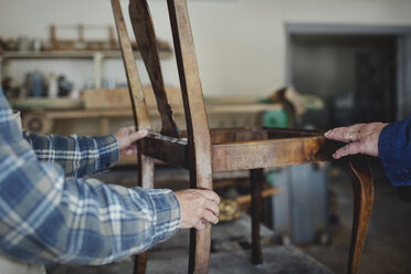 Ausgeschnittenes Bild des Eigentümers, der einem Kunden in der Werkstatt einen Holzstuhl zeigt - MASF00293