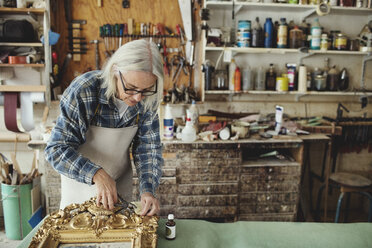 Senior craftsperson working over carved wooden frame at table in workshop - MASF00296