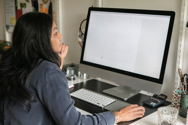 Seitenansicht einer Geschäftsfrau, die einen Computer benutzt, während sie im Büro zu Hause sitzt - MASF00304