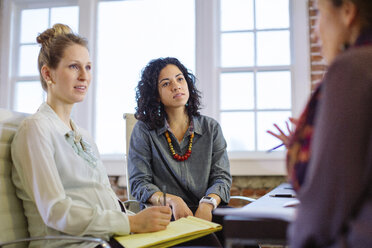 Weibliche Kollegen diskutieren am Schreibtisch sitzend im Büro - CAVF34458