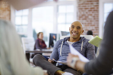 Smiling businessman sitting on chair with colleagues at office - CAVF34466