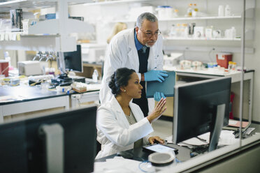 Female doctor discussing with male doctor in medical room seen through glass - CAVF34477