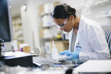 Female doctor examining petri dish at desk in medical room - CAVF34481