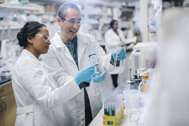 Doctors examining test tubes while coworker working in background at laboratory - CAVF34489