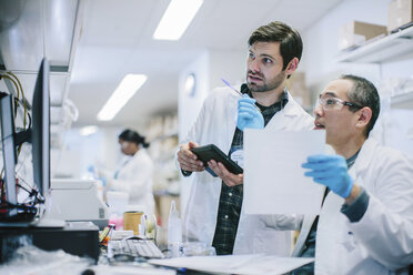 Male doctors discussing reports at desk with female coworker in background - CAVF34495