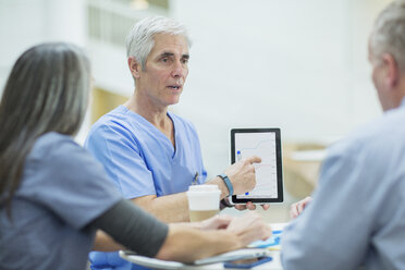 Männlicher Arzt erklärt Mitarbeitern über Tablet-Computer in einer Besprechung im medizinischen Raum - CAVF34535