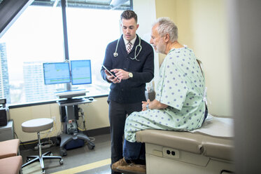 Männlicher Arzt erklärt einem Patienten über einen Tablet-Computer auf der Krankenstation - CAVF34544