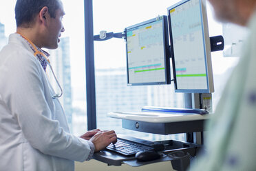 Male doctor using computer while standing by patient in hospital ward - CAVF34545