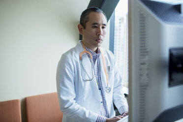 Confident male doctor using desktop computer in hospital ward - CAVF34547