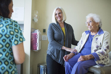 Smiling female patient with daughter looking at doctor while sitting in hospital ward - CAVF34556