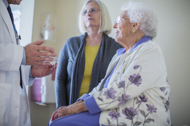 Male doctor talking to female patient sitting by daughter in hospital ward - CAVF34560