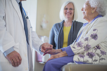 Ein männlicher Arzt hält seine Hand und spricht mit einer Patientin, die neben ihrer Tochter auf der Krankenstation sitzt - CAVF34561