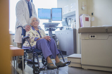 Niedriger Ausschnitt eines Arztes, der neben einem im Rollstuhl sitzenden Patienten im Krankenhaus steht - CAVF34562