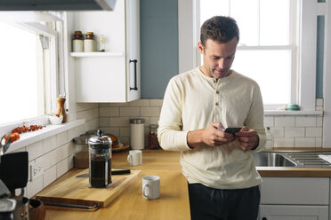 Mann benutzt Smartphone, während er sich zu Hause an die Küchentheke lehnt - CAVF34573