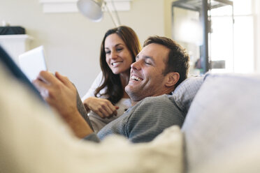Happy couple using digital tablet while relaxing on sofa at home - CAVF34583