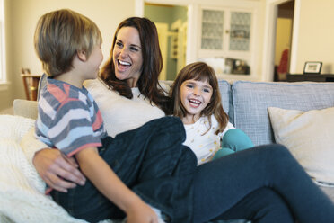 Fröhliche Mutter mit Kindern, die zu Hause auf dem Sofa sitzen - CAVF34593