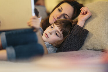 Mother and daughter using tablet computer while lying on sofa at home - CAVF34610