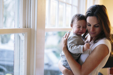 Mutter mit Baby steht am Fenster zu Hause - CAVF34614