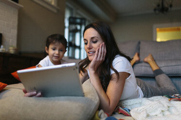 Mädchen schaut Mutter an, die zu Hause einen Tablet-Computer benutzt - CAVF34616