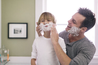 Father applying shaving cream to son in bathroom - CAVF34622