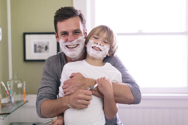 Portrait of happy father and son with shaving cream on face standing in bathroom - CAVF34623