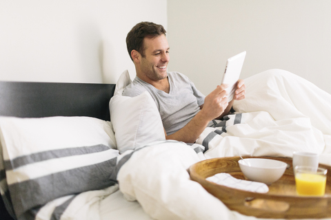 Mann benutzt Tablet-Computer, während er zu Hause auf dem Bett sitzt, lizenzfreies Stockfoto