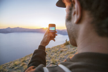 Hiker photographing with mobile phone at Crater Lake National park during sunset - CAVF34657