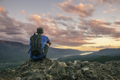 Rear view of hiker with backpack sitting on mountain at Crater Lake National Park - CAVF34659