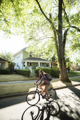 Full length of woman cycling on road against houses - CAVF34666