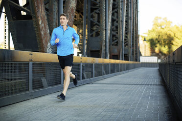 Full length of man running while exercising on bridge in city - CAVF34668