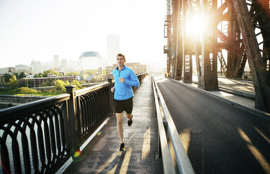 Man running while exercising on bridge against clear sky in city - CAVF34674