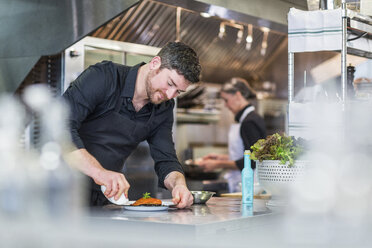 Koch garniert Essen, während eine Mitarbeiterin im Hintergrund im Restaurant arbeitet - CAVF34699