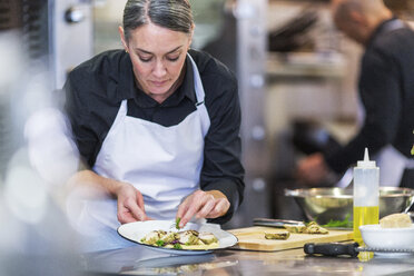 Female chef garnishing food while coworker working in background at restaurant - CAVF34701