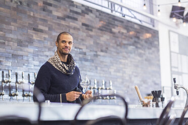 Bartender looking away while holding wineglass at bar counter in restaurant - CAVF34712