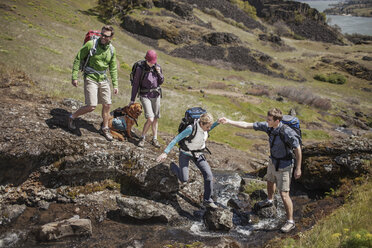 Man assisting friend while crossing stream on mountain - CAVF34850