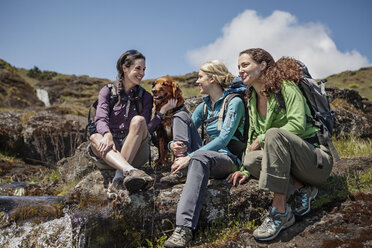 Happy female hikers talking while sitting with dog on hill - CAVF34852
