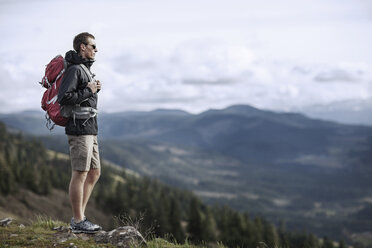 Hiker carrying backpack while standing on mountain against sky - CAVF34868