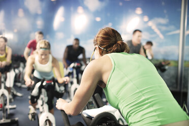 Fitness instructor with clients riding exercise bikes at gym - CAVF34880