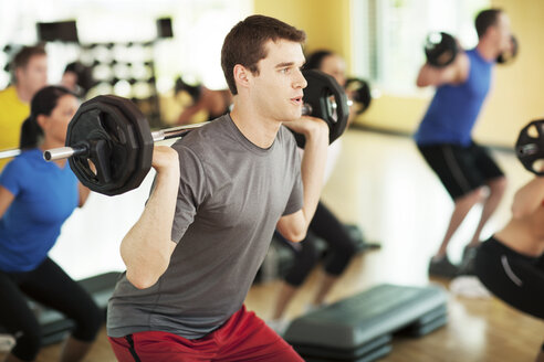 Männlicher Sportler hebt eine Langhantel im Fitnessstudio - CAVF34885