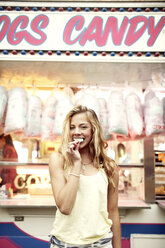 Porträt einer glücklichen Frau, die Zuckerwatte an einem Stand in einem Vergnügungspark isst - CAVF34906