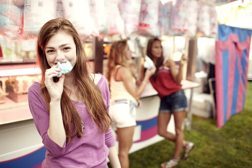 Porträt eines Teenagers, der mit Freunden im Hintergrund Zuckerwatte isst - CAVF34907