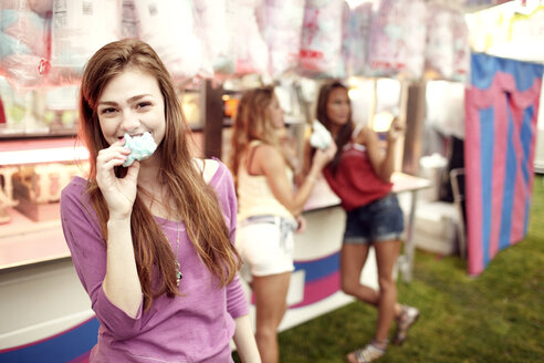 Portrait of teenage girl eating cotton candy with friends in background - CAVF34907