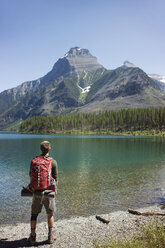 Rückansicht eines Mannes mit Rucksack, der am Seeufer im Glacier National Park steht - CAVF34911