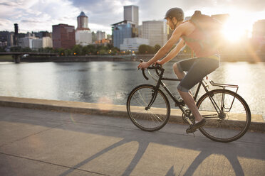 Man carrying backpack while riding bicycle on street during sunset - CAVF34926