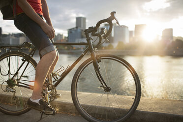 Low section of man riding bicycle on street by lake during sunset - CAVF34927