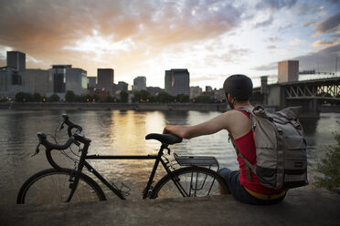 Athlete carrying backpack while sitting on retaining wall by lake - CAVF34928