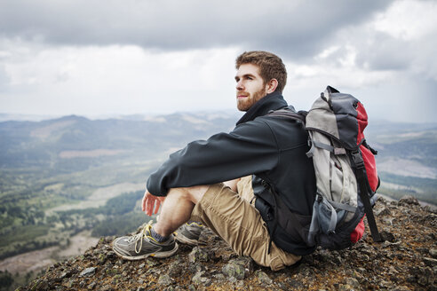 Nachdenklicher Mann mit Rucksack auf einem Berg sitzend - CAVF34933