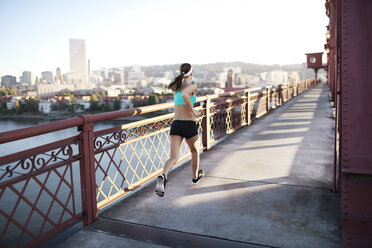 Rückansicht einer entschlossenen sportlichen Frau, die auf einer Brücke läuft - CAVF34944